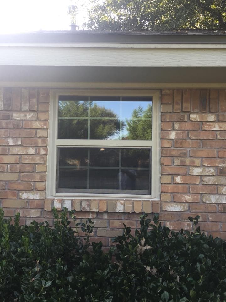 A light-colored window frame and divided glass set into an existing brick exterior